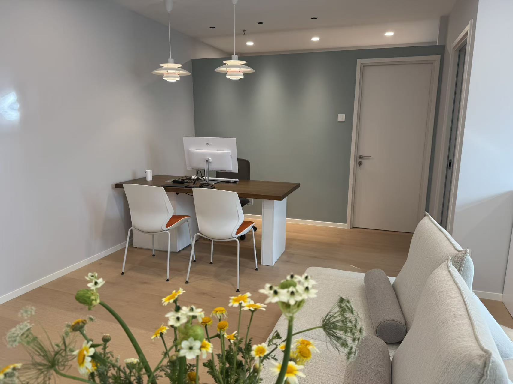 A calm, light-filled consultation room at Younuoya with sage-green walls, soft seating and fresh flowers